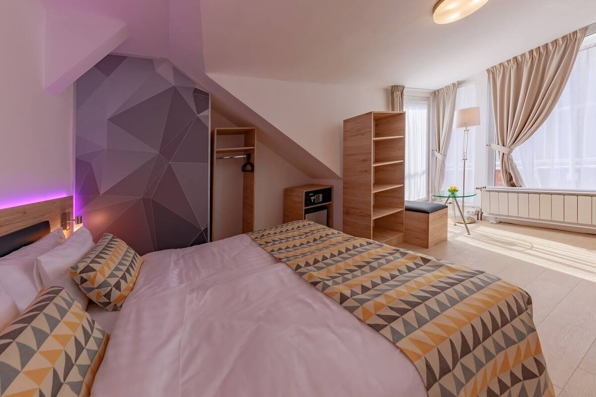 A bedroom with a bed, a wardrobe, a desk, and a window with curtains.