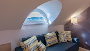 A modern room with a curved ceiling skylight, a dark sofa with patterned cushions, and a geometric wall design. - Christina Residence (Budapest)