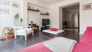 A modern living room with a white sofa, a red coffee table, a white armchair, a TV, and a kitchen area visible through an open doorway. - FLH Príncipe Real Design Flat (Lisbon)