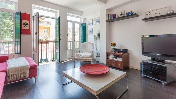 A modern living room with a sofa, a red table, a TV, and a balcony door. - FLH Príncipe Real Design Flat (Lisbon)