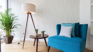 A modern living room with a blue sofa, a round wooden side table, a floor lamp, and a potted plant.