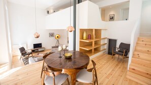 A spacious living area with a round wooden table, multiple chairs, a television, and a bookshelf. - FLH Santa Catarina Modern Place (Lisboa ciudad)