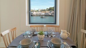A dining table set with plates, glasses, and cutlery, overlooking a cityscape and river. - FLH Luxury Porto River View (Vila Nova de Gaia)