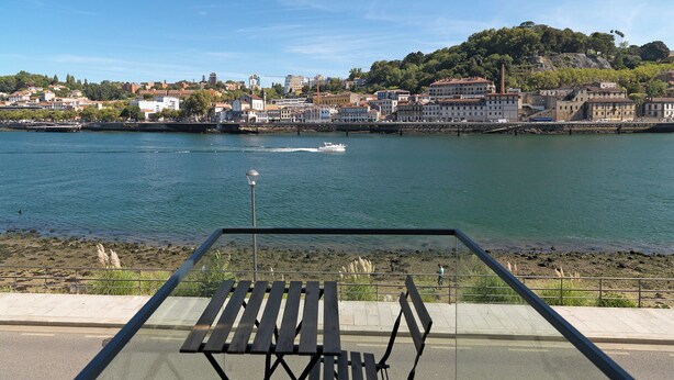 A riverside view with a bench overlooking the water, a boat passing by, and buildings along the riverbank. - FLH Luxury Porto River View (Vila Nova de Gaia)