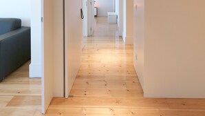 A modern hallway with wooden flooring, white walls, and a sofa on the left. - FLH Luxury Porto River View (Vila Nova de Gaia)