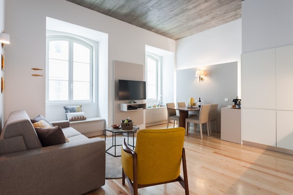 A modern living room with a sofa, a yellow armchair, a TV, and a dining area with chairs and a table.