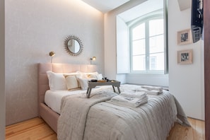 A bedroom with a bed, bedside lamps, a window, and a mirror on the wall.