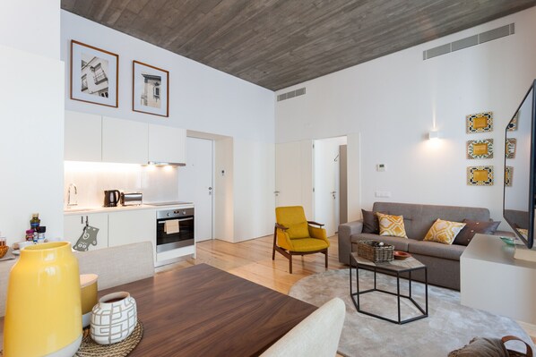 A modern living room with a sofa, coffee table, and a yellow armchair. There is a kitchen area with a toaster and a kettle. - FLH Alecrim Modern Flat (Lisbon)