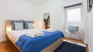 Un dormitorio con cama, una silla, un ventanal y una planta pequeña.