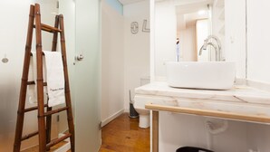 Un baño con una escalera de madera, un lavamanos blanco y un espejo.