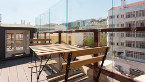 A balcony with a wooden table and chairs, a glass railing, and a view of buildings in the background. - FLH Santa Marta Cozy Flat (Lisbon)