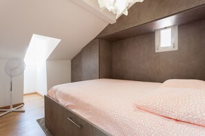 Une chambre à coucher avec un lit, une petite fenêtre et un ventilateur sur pied.