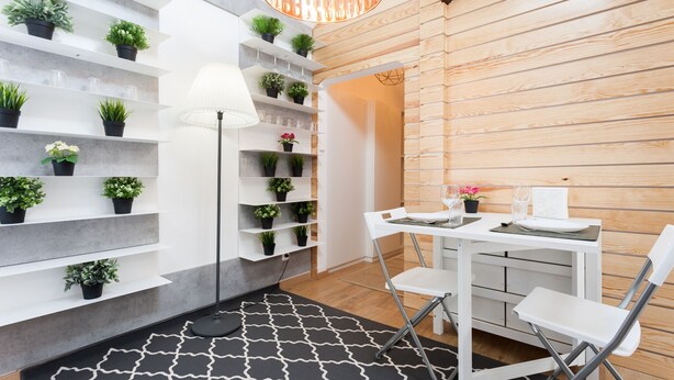 A modern room with a white table and chairs, a black and white patterned rug, and shelves with potted plants. - FLH Santa Marta Cozy Flat (Lisbon)
