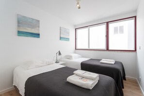 A hotel room with two beds, a large window, and artwork on the wall.