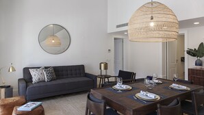 A modern living room with a dark grey sofa, a round mirror, and a dining table set for four. - FLH Restauradores Luxus Flat (Lisbon)