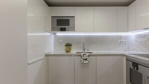 A modern kitchen with white cabinetry, a stainless steel oven, and a built-in microwave above the sink. - FLH Restauradores Luxus Flat (Lisbon)