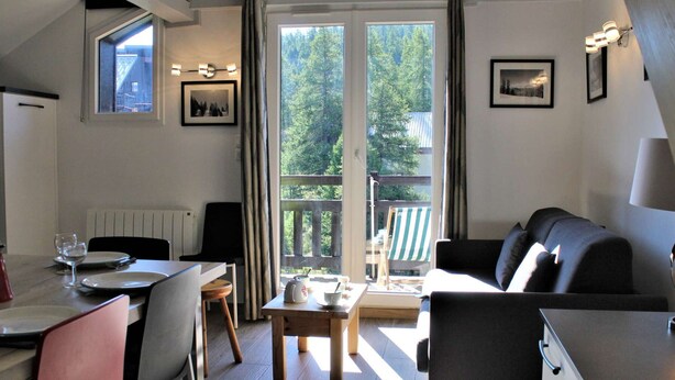 Une pièce chaleureuse comprenant une table à manger, des chaises, un canapé et une vue sur une forêt, visible à travers une grande fenêtre.