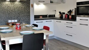 Une cuisine moderne avec des meubles blancs, un plan de travail noir et un four encastré. On y trouve une table à manger avec des chaises et une tasse rouge.