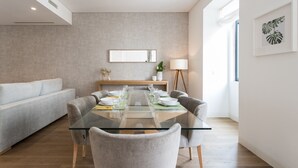 Ein moderner Essbereich mit einem Glastisch, grau gepolsterten Stühlen und einem grauen Sofa.