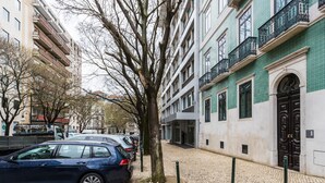 Eine gepflasterte Straße, gesäumt von parkenden Autos und Gebäuden mit Balkonen.