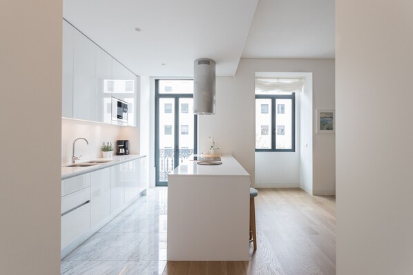 A modern kitchen with white cabinetry, a central island, and a large window providing natural light.
