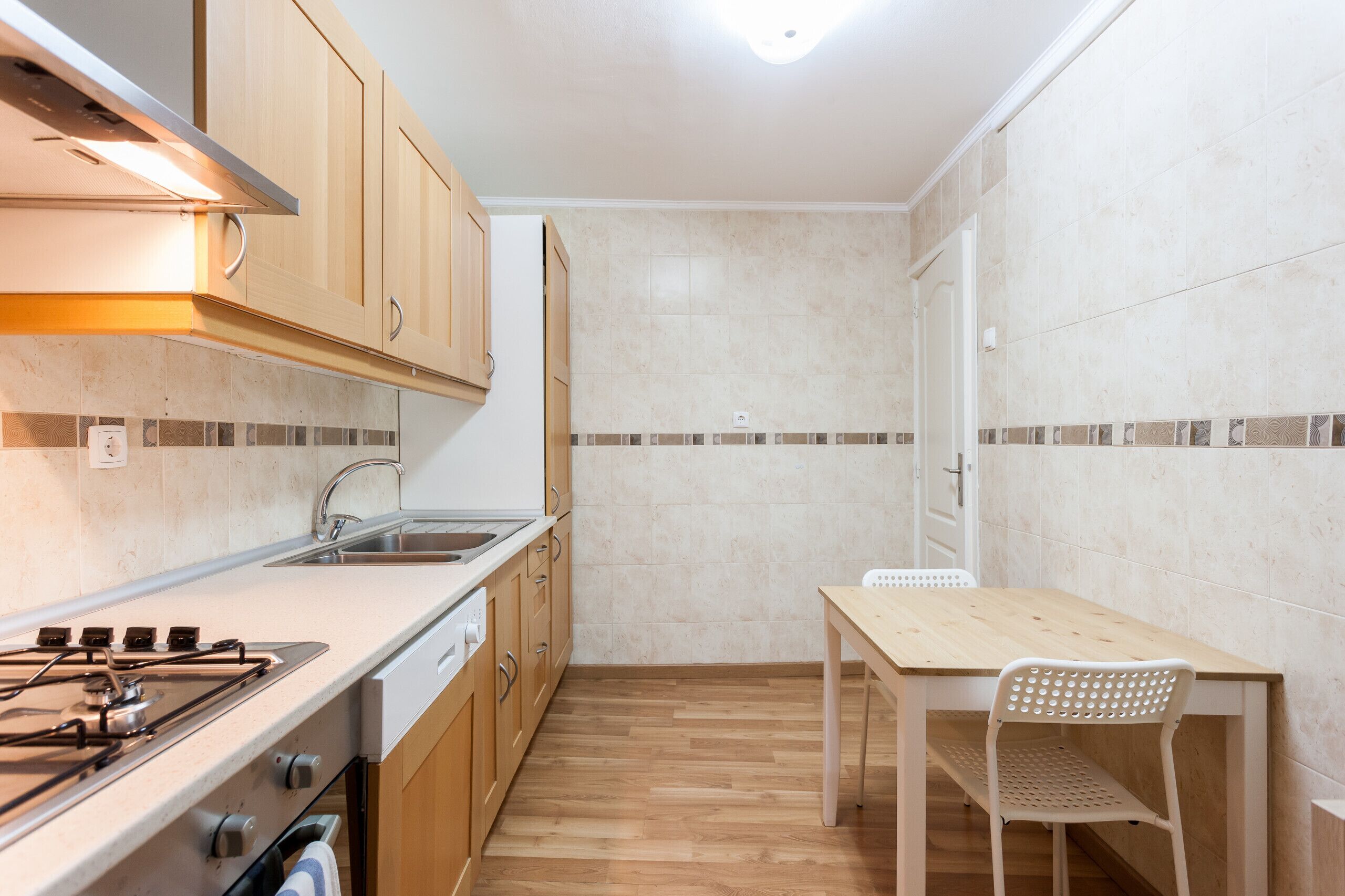 Une cuisine compacte avec des meubles en bois, une cuisinière à gaz, un évier et une petite table à manger avec une chaise.