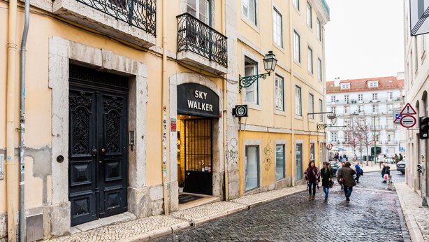 A cobblestone street with a building featuring a black ornate door and a sign reading "SKY WALKER". - FLH Bairro Alto Stylish Apartment (Lisbon)