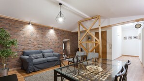 A modern living room with a brick wall, a gray sofa, a glass dining table, and a wooden ceiling structure. - FLH Bairro Alto Stylish Apartment (Lisbon)