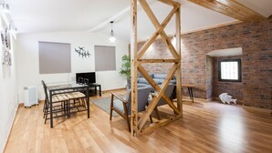 A spacious room with a wooden ceiling structure, a dining area with a table and chairs, a gray sofa, and a brick wall. - FLH Bairro Alto Stylish Apartment (Lisbon)