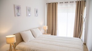 Una cama bien tendida con ropa de cama blanca, una lámpara de noche y una mesita de noche.