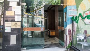 Entrada de hotel con puertas de vidrio, piso de baldosas y una pared con varias placas y un mural.