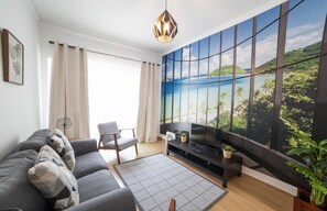 Una sala de estar moderna con un ventanal grande, un sofá gris, un mueble de entretenimiento negro y una lámpara colgante.