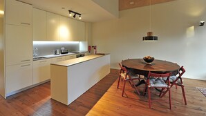 A modern kitchen with white cabinets, a wooden dining table, and red chairs. - FLH Oporto Captain House - Calem Apartment (Oporto)