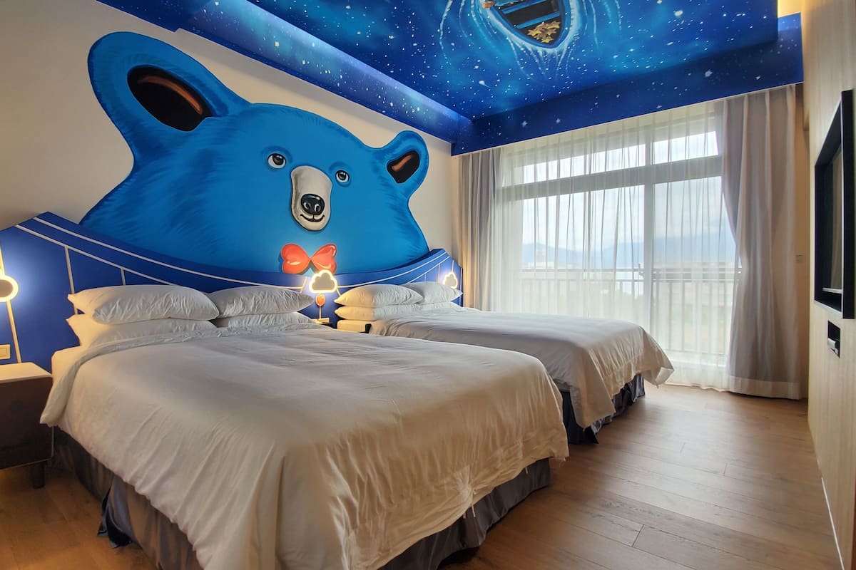 A hotel room with two beds, a large bear mural on the ceiling, and a view of the outdoors through the window.