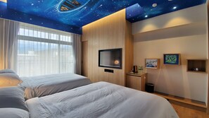 Habitación de hotel con diseño de techo estrellado, dos camas, un televisor y una mesita con un marco de fotos y un cesto de basura.