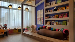 Una habitación acogedora con un ventanal grande, una estantería llena de libros, un sillón de felpa colorido y una pequeña mesa con juguetes.