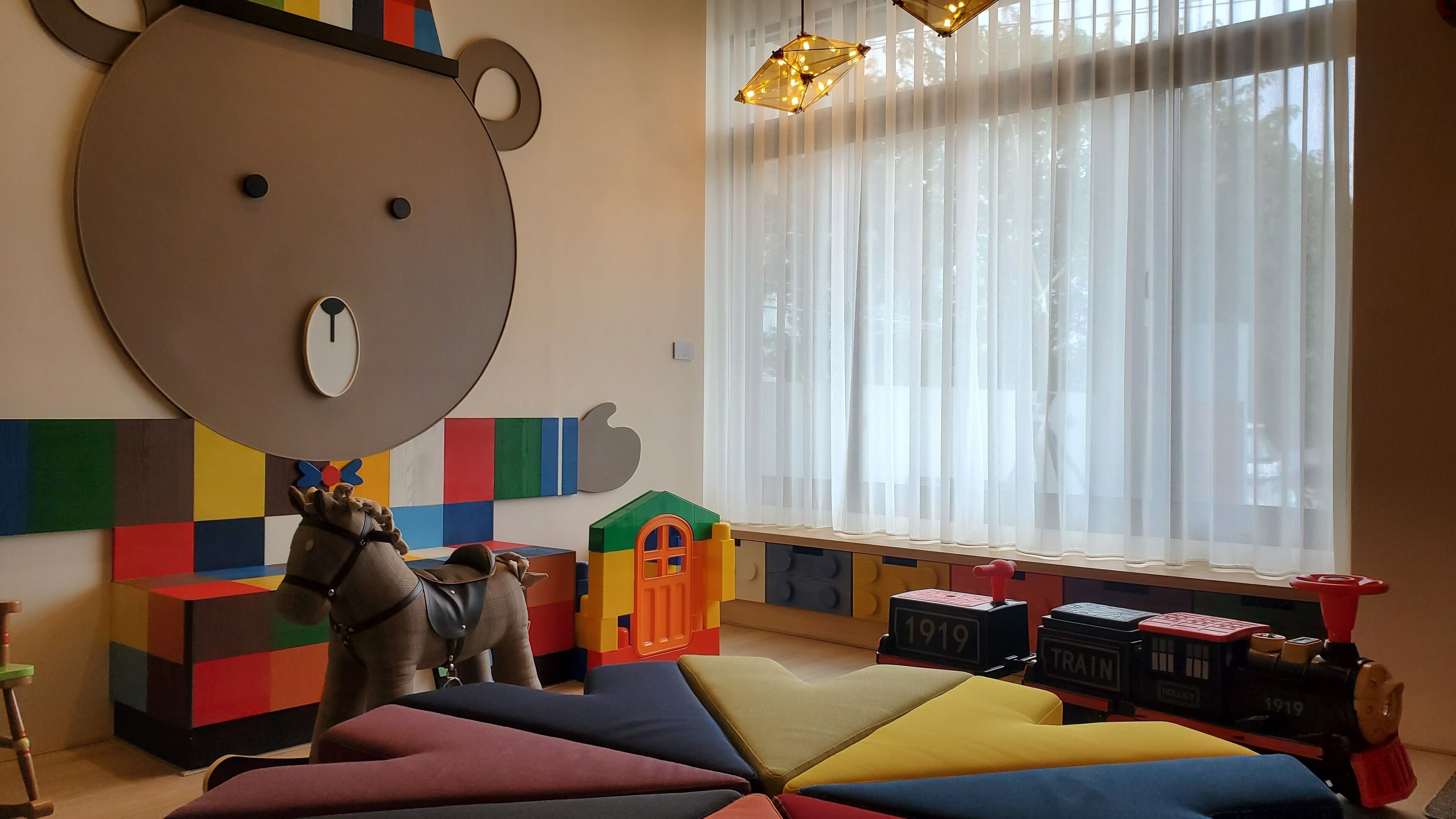 Un cuarto de juegos para niños con una gran decoración de oso, bloques de colores y un tren de juguete.