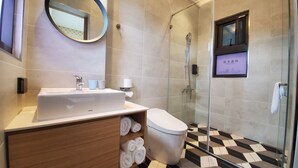 Un baño moderno con lavamanos, espejo y retrete blancos. Cuenta con un box de ducha de vidrio y un suelo a cuadros blanco y negro.