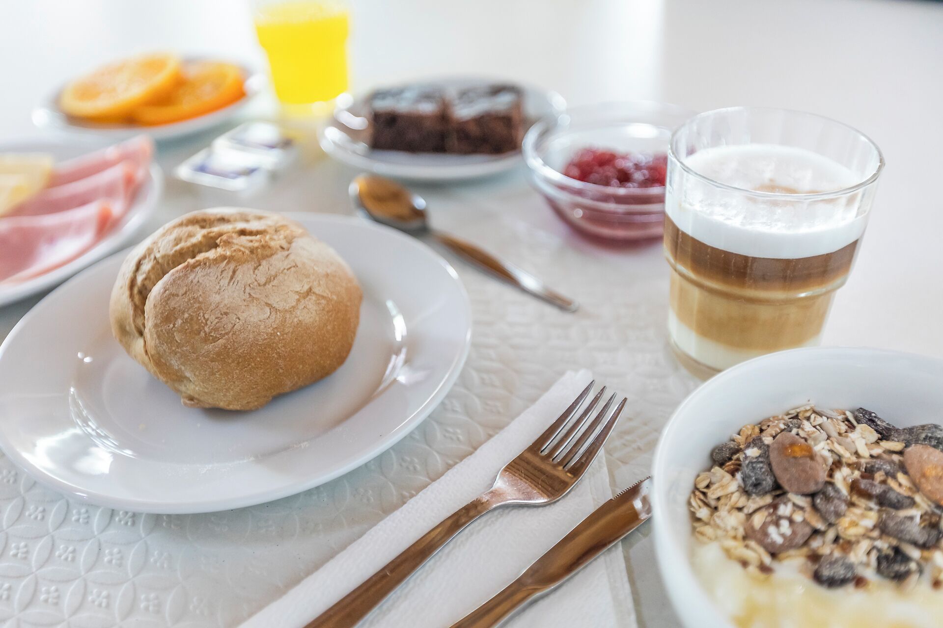 Una tavola da colazione con dolci, un bicchiere di succo, una ciotola di cereali e una tazza di caffè.