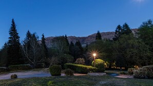 Paisaje nocturno con una montaña, árboles y un jardín bien iluminado.