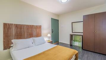 A hotel room with a bed, a desk with a chair, a wardrobe, and a green door.