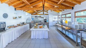 Cocina amplia con vigas de madera, mesa de buffet y vistas al exterior a través de grandes ventanales.