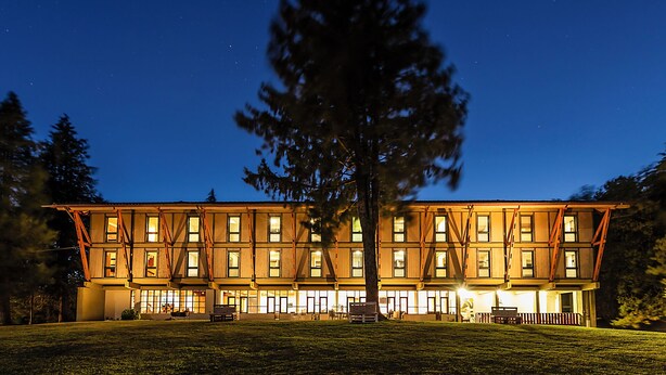 Un edificio de varios pisos con amplios ventanales, un árbol central y un césped bien iluminado.