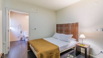 A hotel room with a bed, bedside table, lamp, and a bathroom visible through an open door.