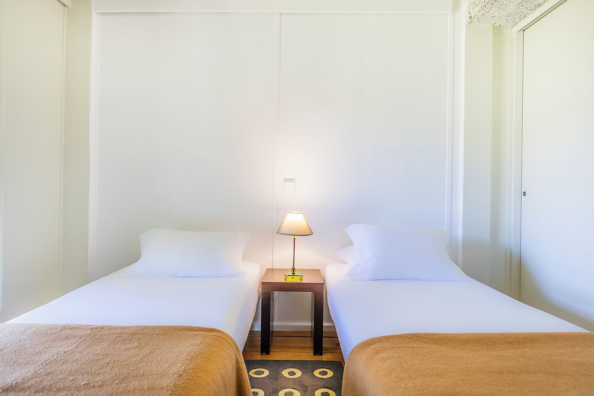 Een hotelkamer met twee bedden, een nachtkastje met een lamp en een klein tafeltje.