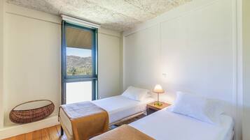 Una habitación con dos camas, una ventana con vistas, una lámpara en una mesita de noche y una cesta tejida.