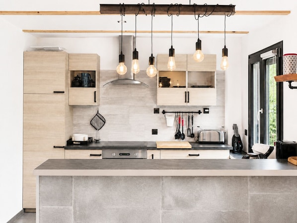 Una cocina moderna con armarios de madera, una isla central, luces colgantes y un ventanal que proporciona luz natural.