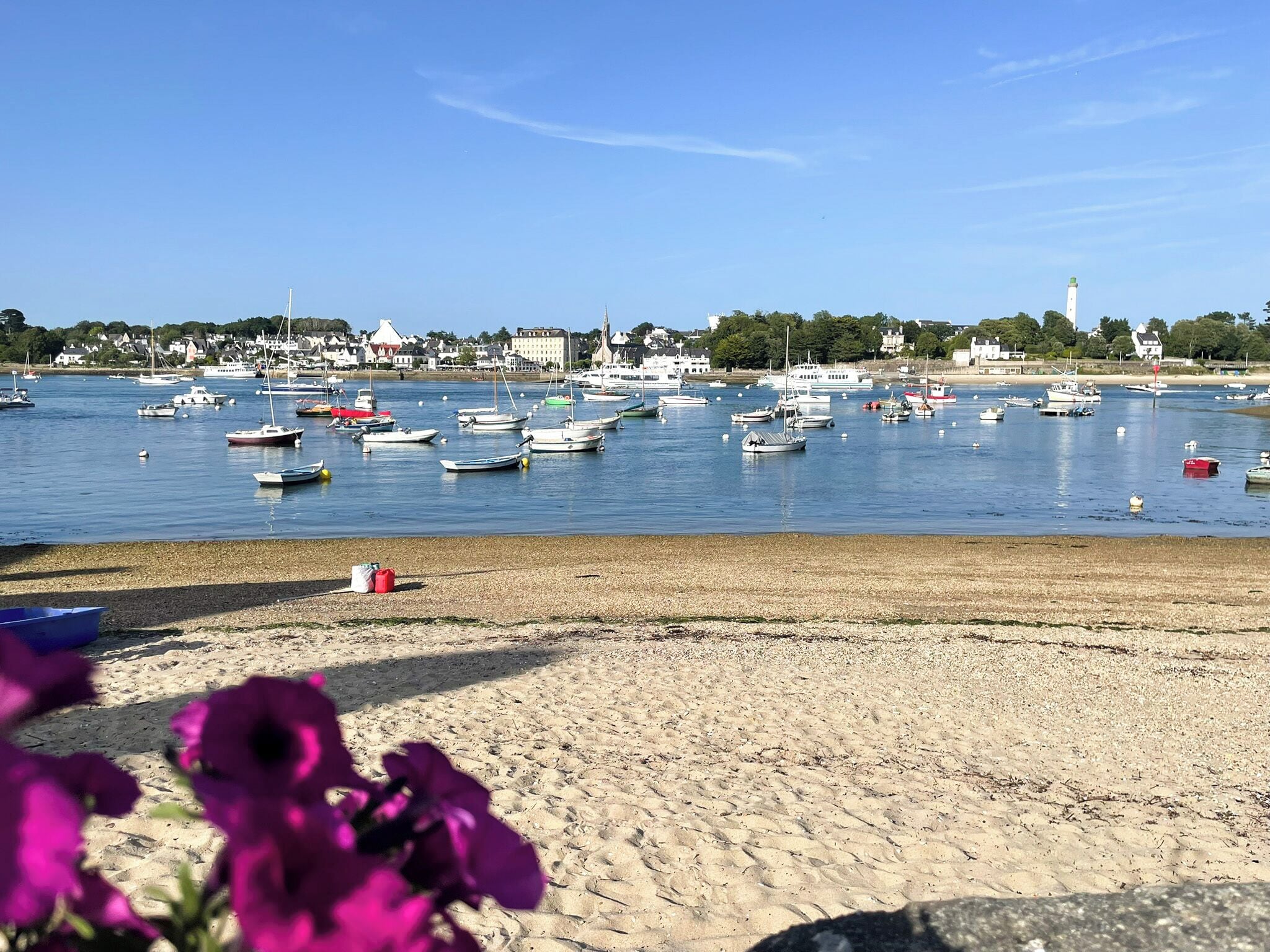 A beach with boats in the water and a town in the background.