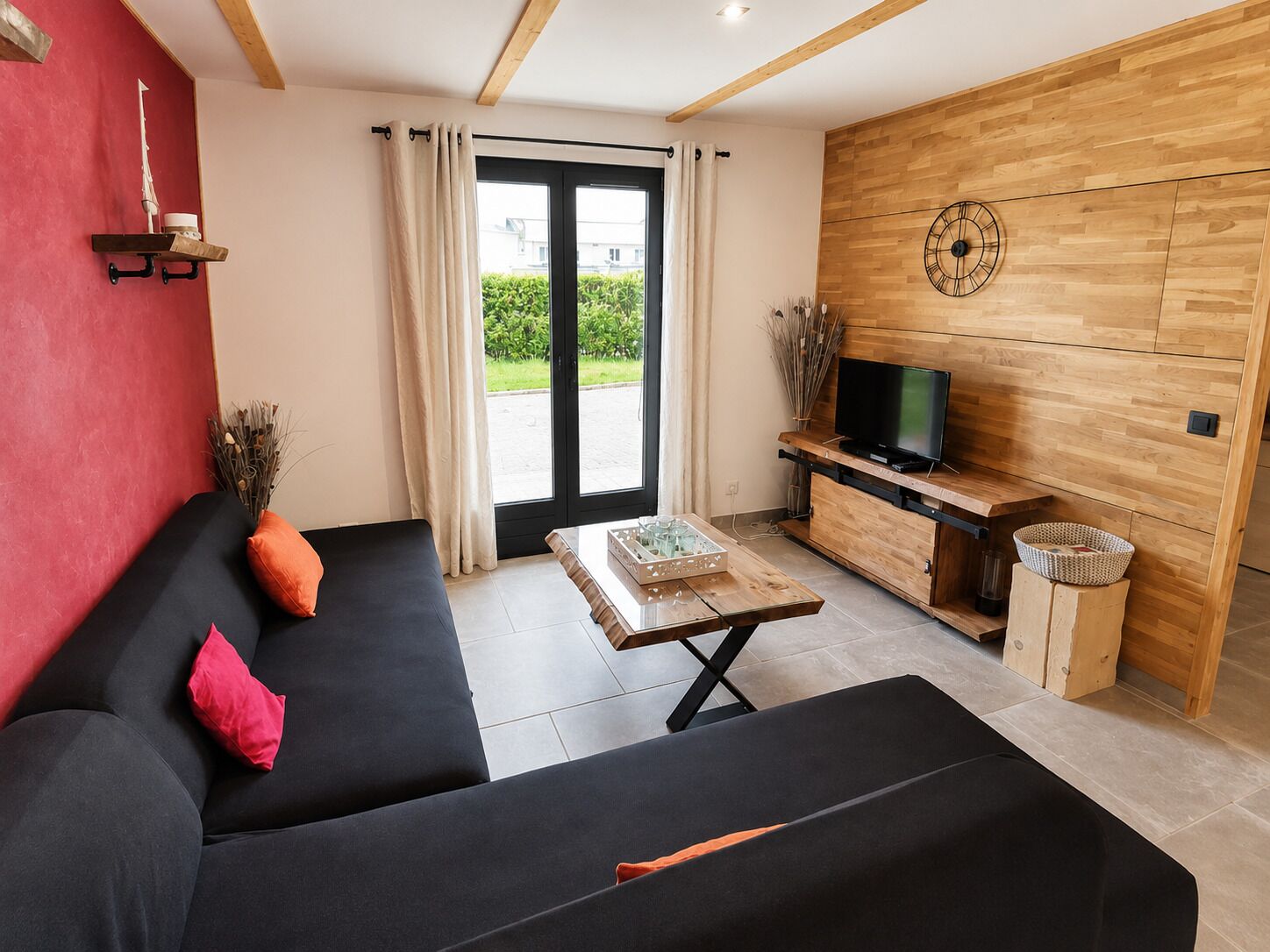 A modern living room with a black sofa, a wooden TV stand, and a large window with curtains.