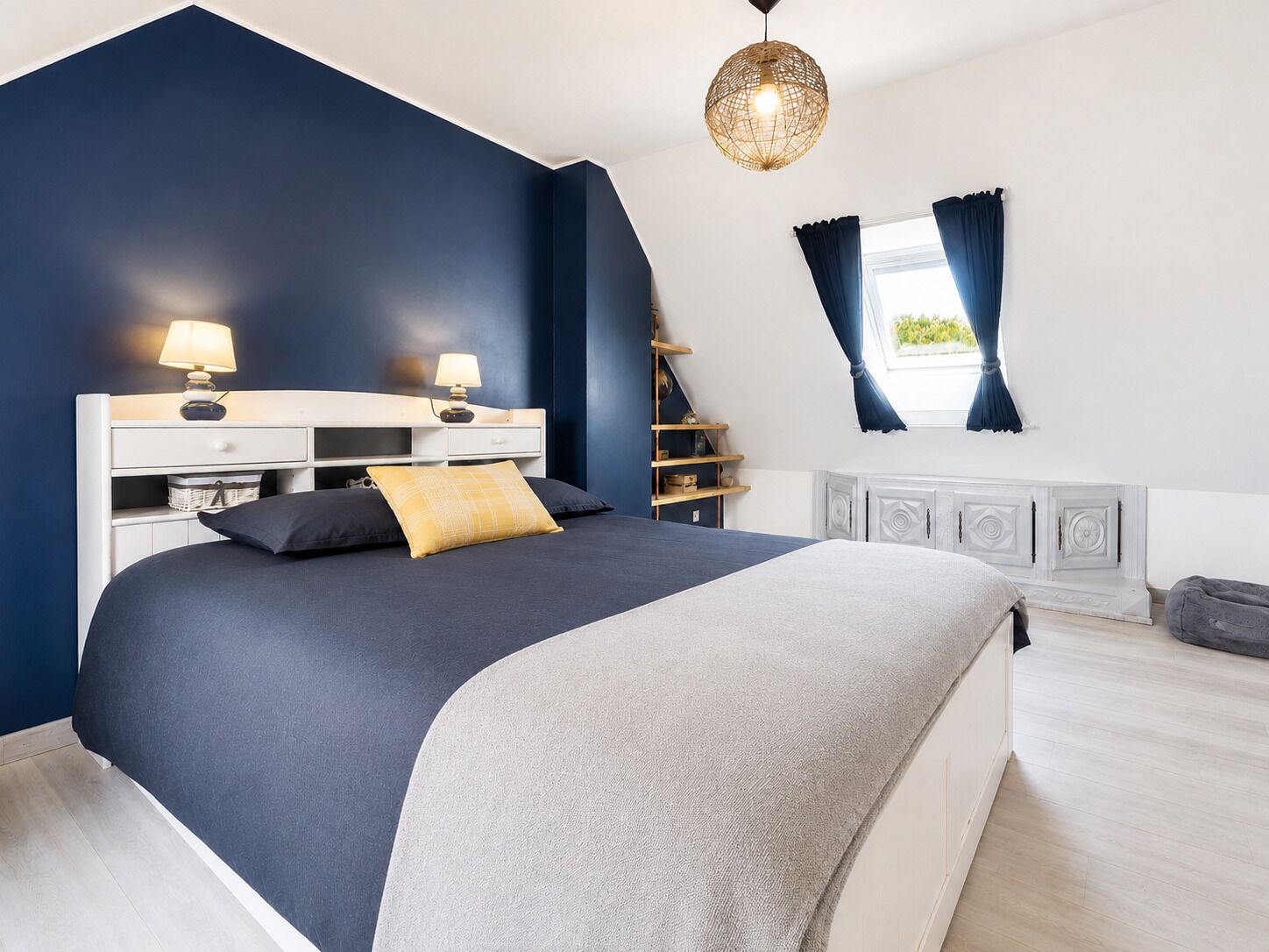 Un dormitorio con una cama, mesitas de noche, una lámpara, una ventana con cortinas y un candelabro colgante.